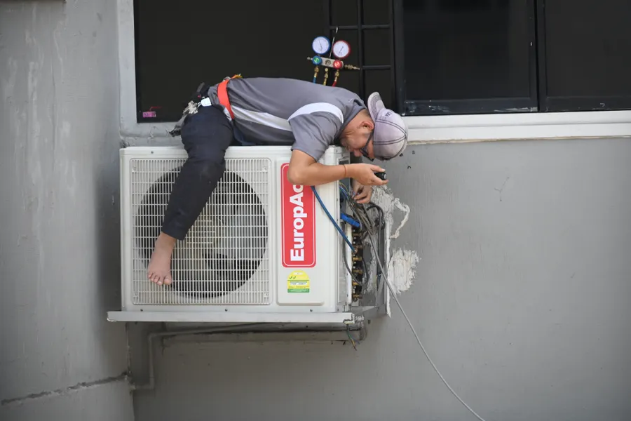 Technician repairing an outdoor air conditioning unit mounted on a building wall