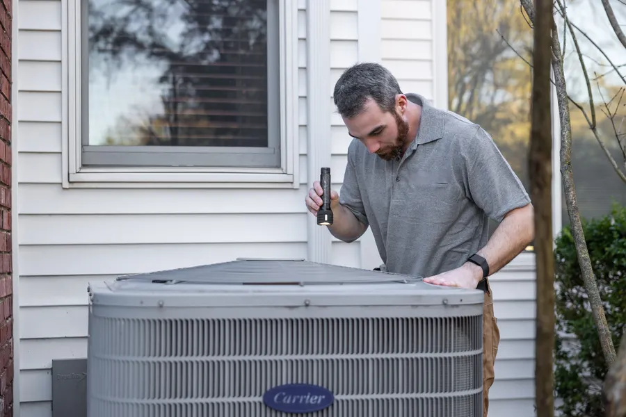 Technician inspecting an outdoor condenser unit during a maintenance visit